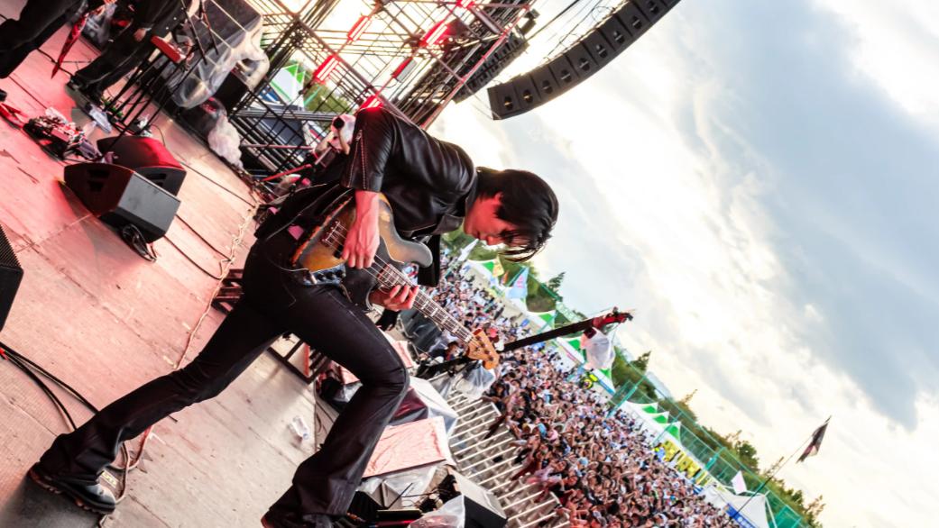 A guitarist performing on an outdoor stage with the crowd beyond