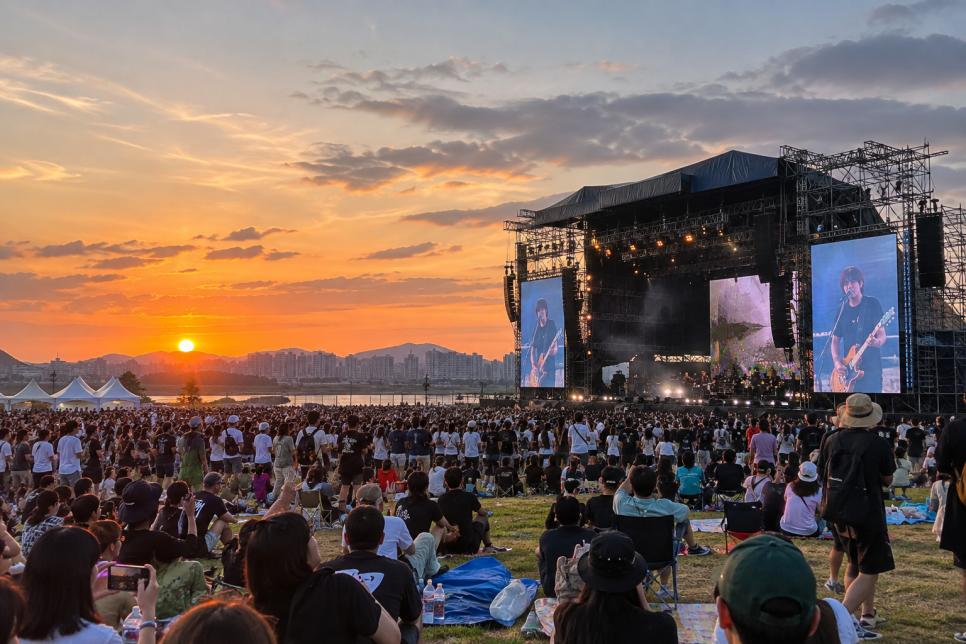 Outdoor rock festival stage and audience beside the river at sunset