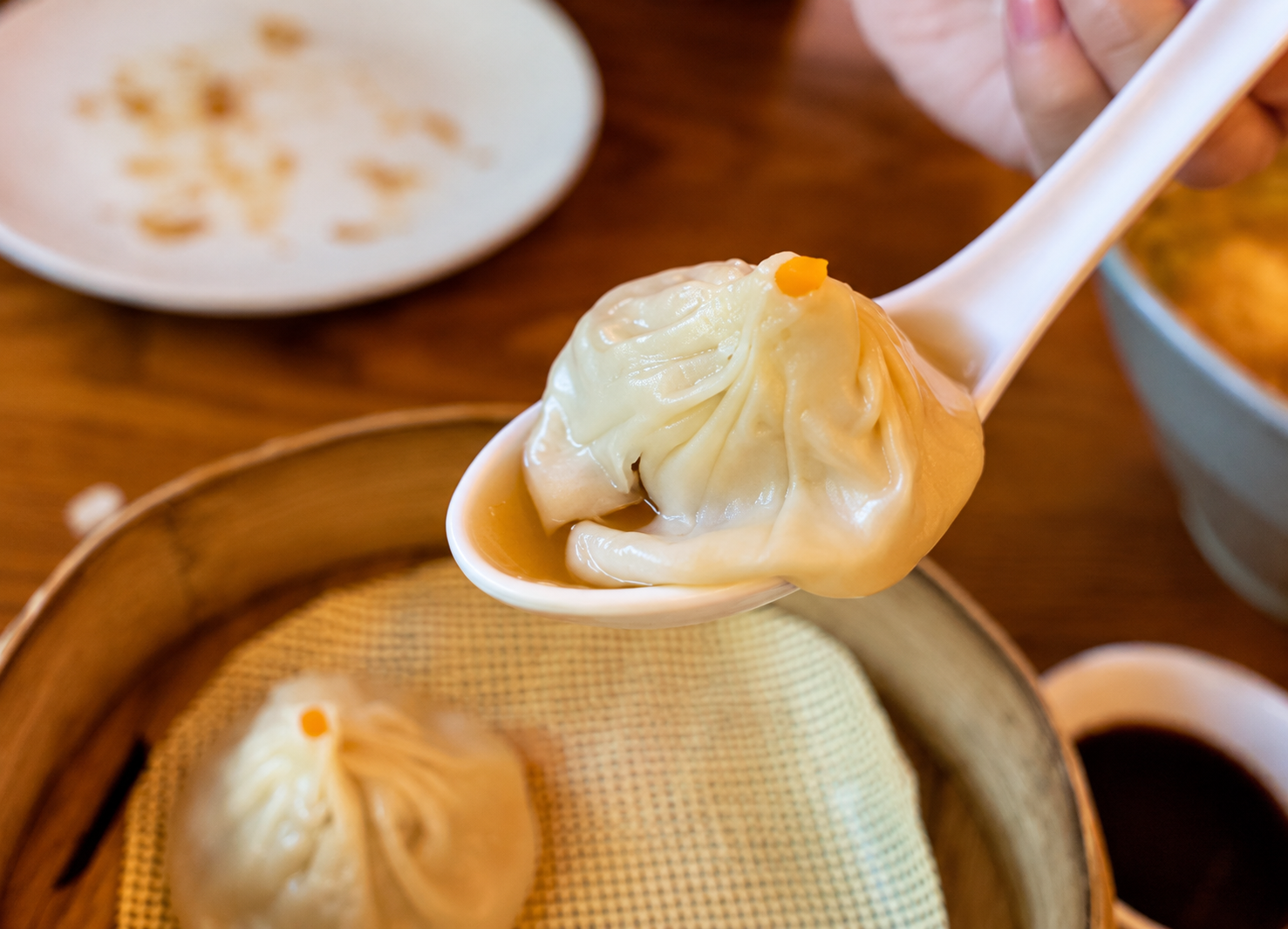 Soup dumpling on a white spoon at Dim Tao — AI-assisted edit