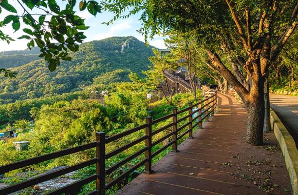 A shaded walking path with a wooden railing on the Seokbulsa approach