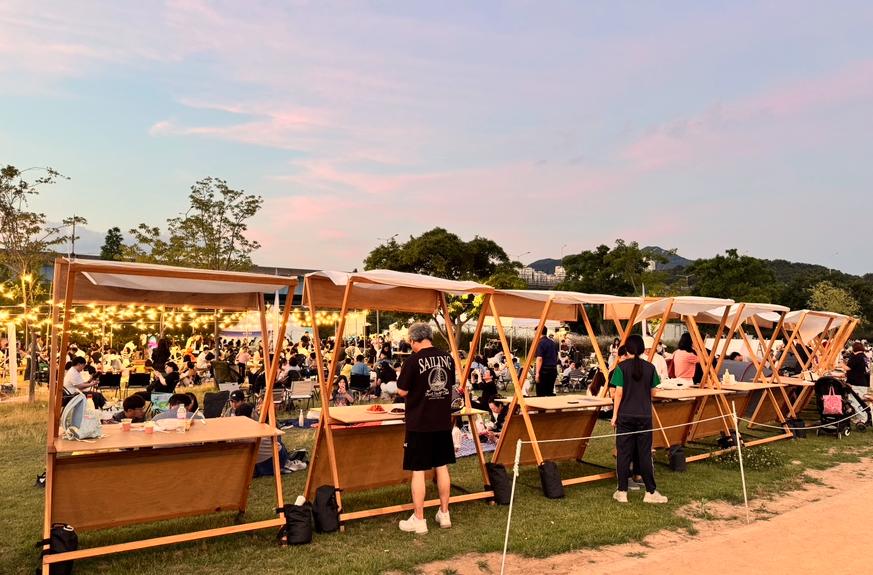 Wooden market stalls with visitors and picnic seating at dusk