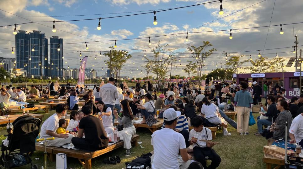 Visitors seated outdoors beside food and Korean liquor stalls