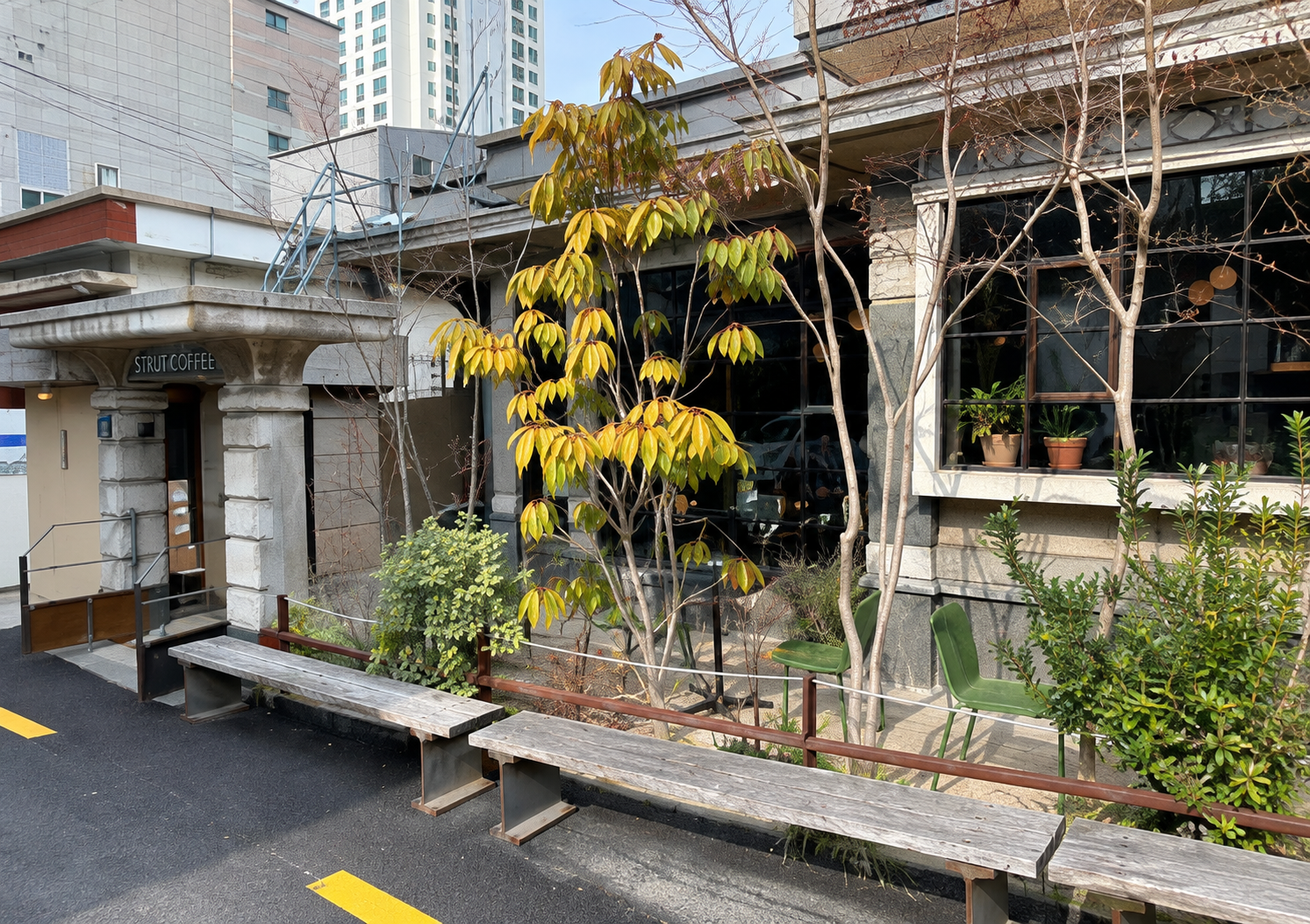 Strut Coffee exterior with trees and a bench — AI-assisted edit