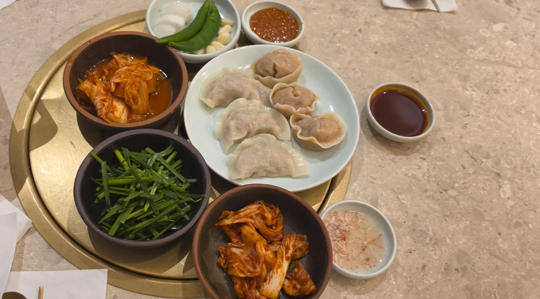 A plate of dumplings surrounded by kimchi, chives, vegetables and dipping sauces at Geodae Dwaeji Gukbap.