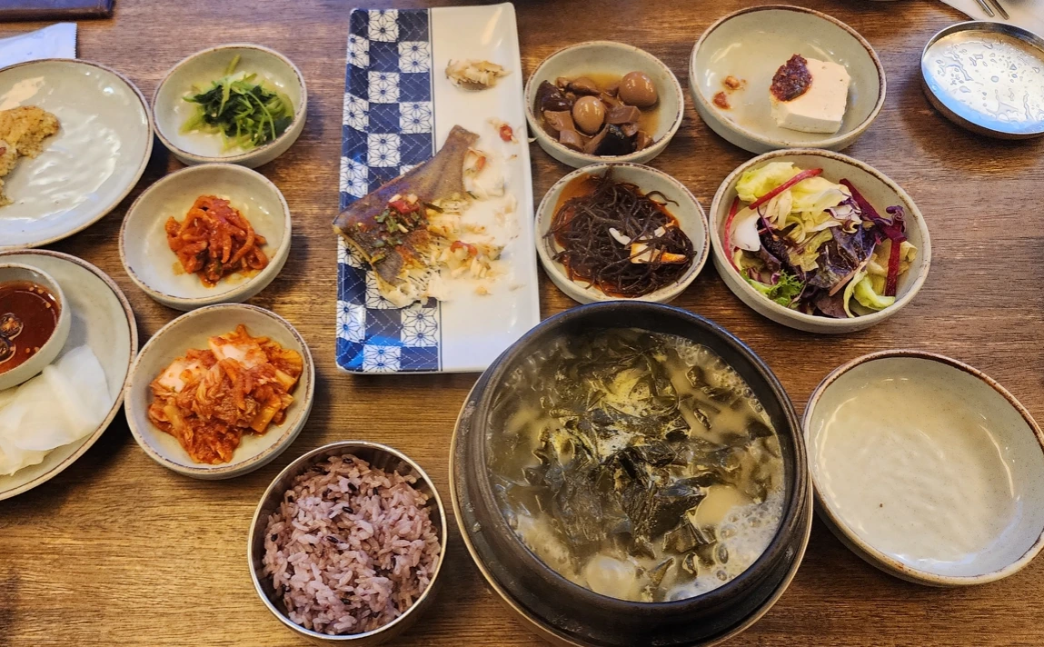 A bowl of seaweed soup with multigrain rice, a fish dish and assorted Korean side dishes.