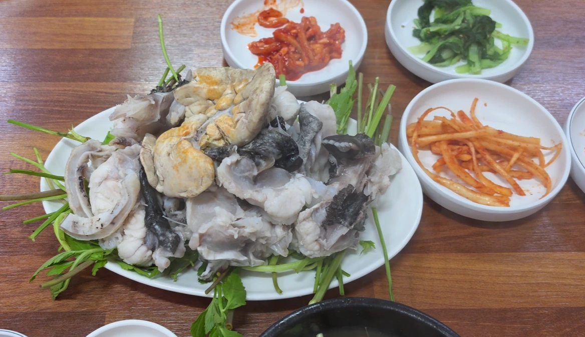 Steamed monkfish and pale monkfish liver piled over minari greens, with Korean side dishes.