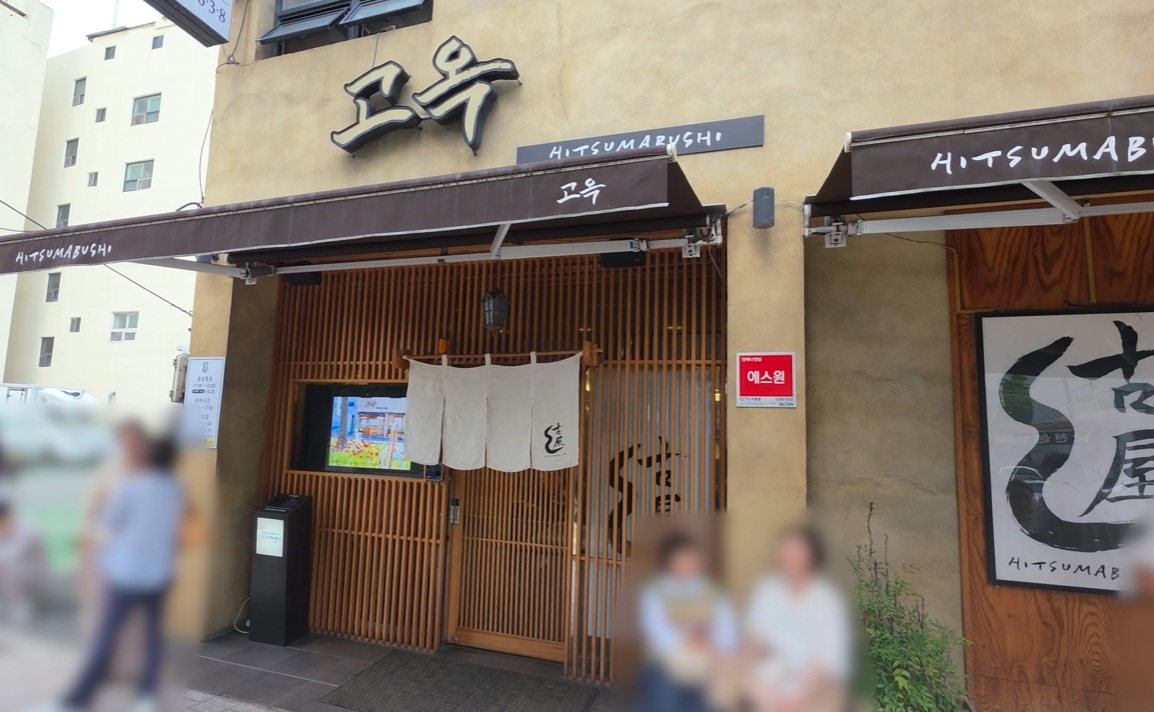 Go-ok restaurant’s wooden entrance and brown hitsumabushi awning, with people blurred in the original video.