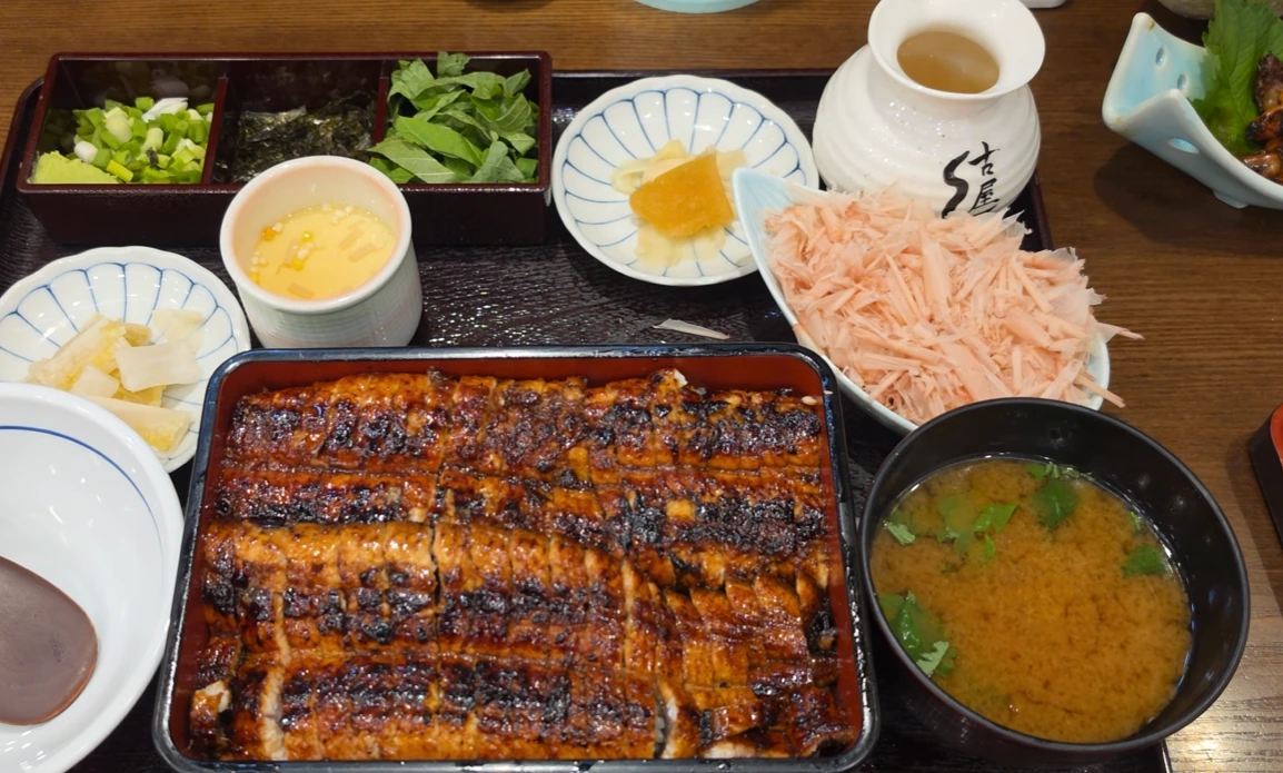A lacquered box filled with grilled eel over rice, served with soup, egg custard, pickles and condiments.
