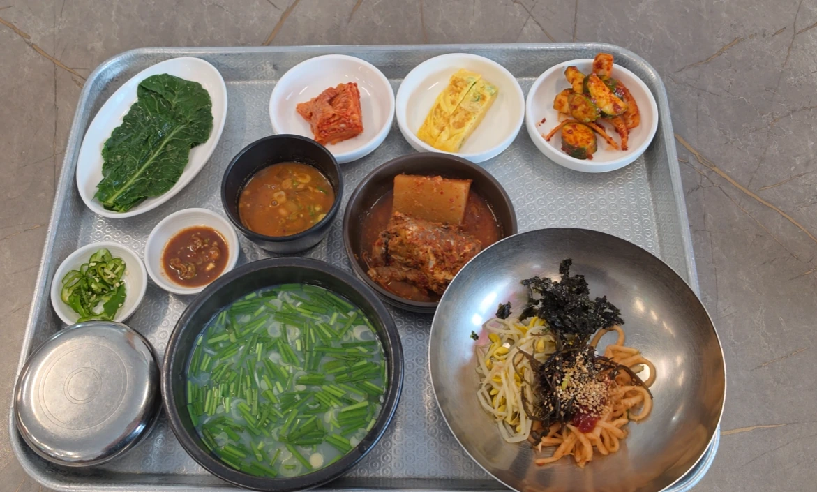 A tray holding chive-topped clam soup, a mixing bowl of vegetables, rice and assorted side dishes.