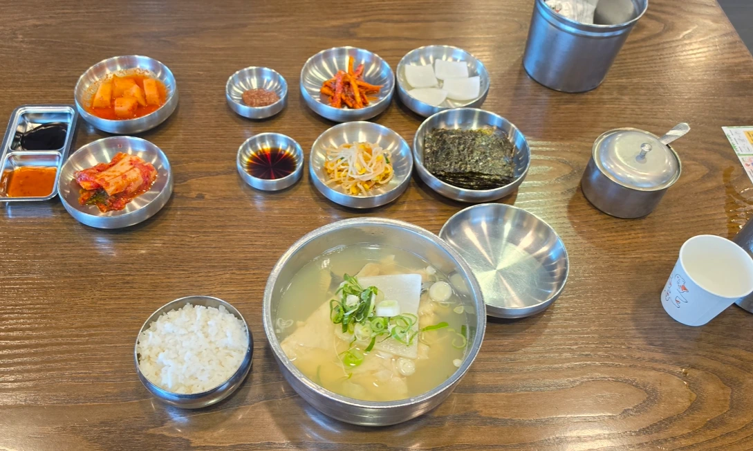 A bowl of cod soup topped with sliced scallions and radish, served with rice, kimchi, seaweed and other side dishes.