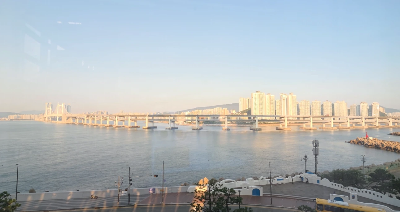 Gwangan Bridge spanning the water, with waterfront apartment towers in warm sunlight.