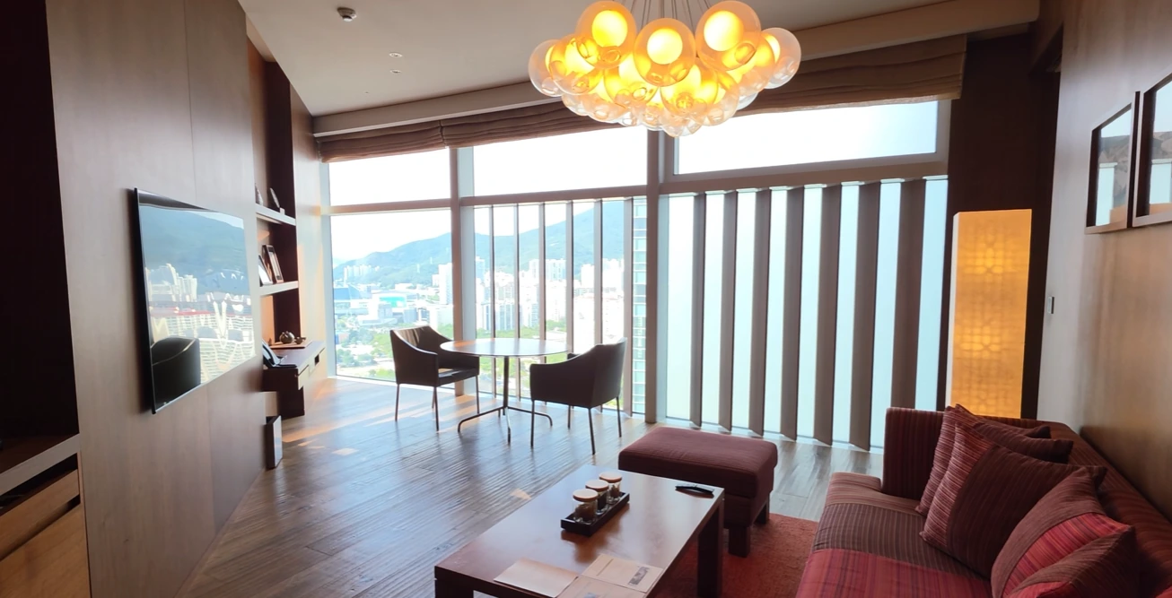 A suite living room with a sofa, coffee table, dining table and tall windows at Park Hyatt Busan.